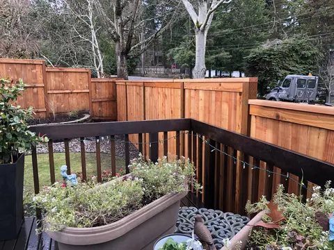 Completed composite deck with black composite railings, built-in curved planter beds, potted plants, and mature trees