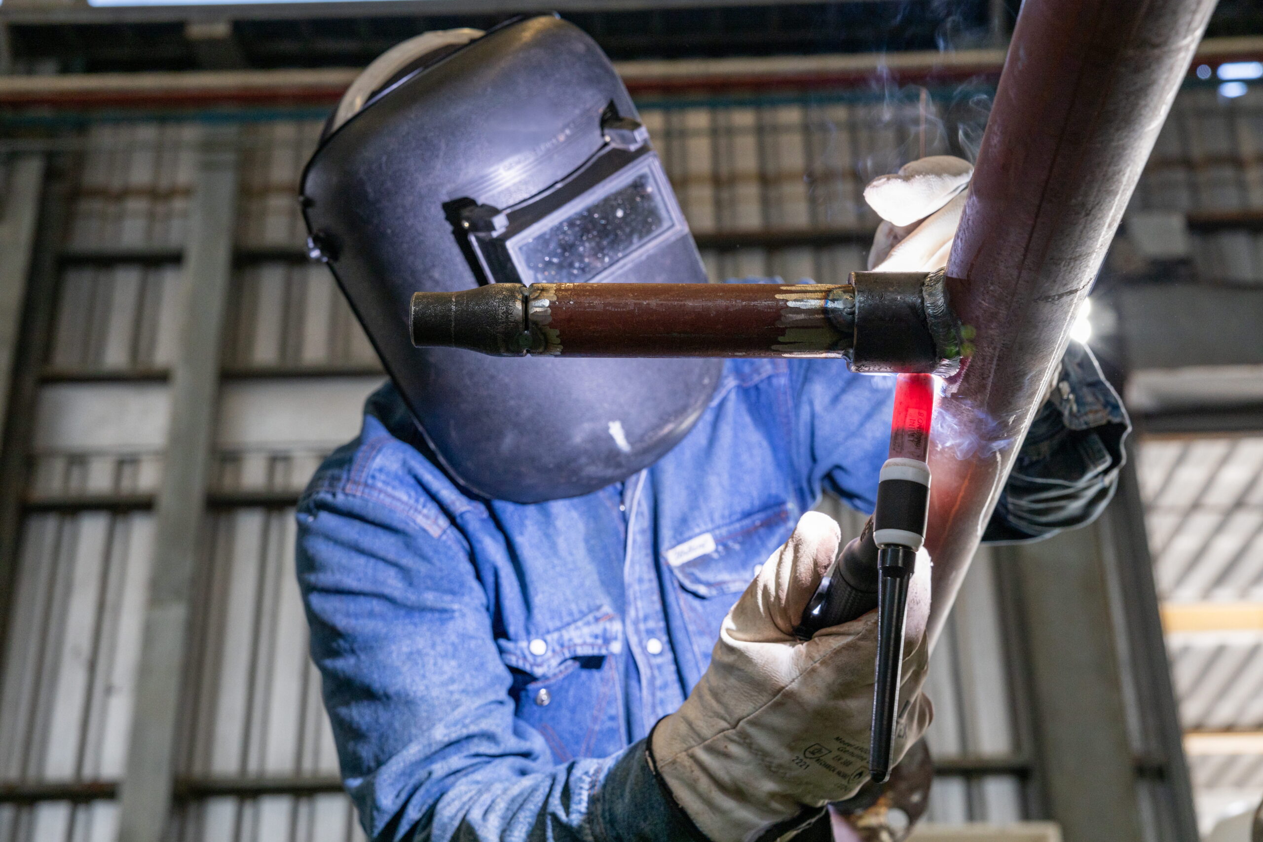 Welder performing structural pipe welding in a metal fabrication shop