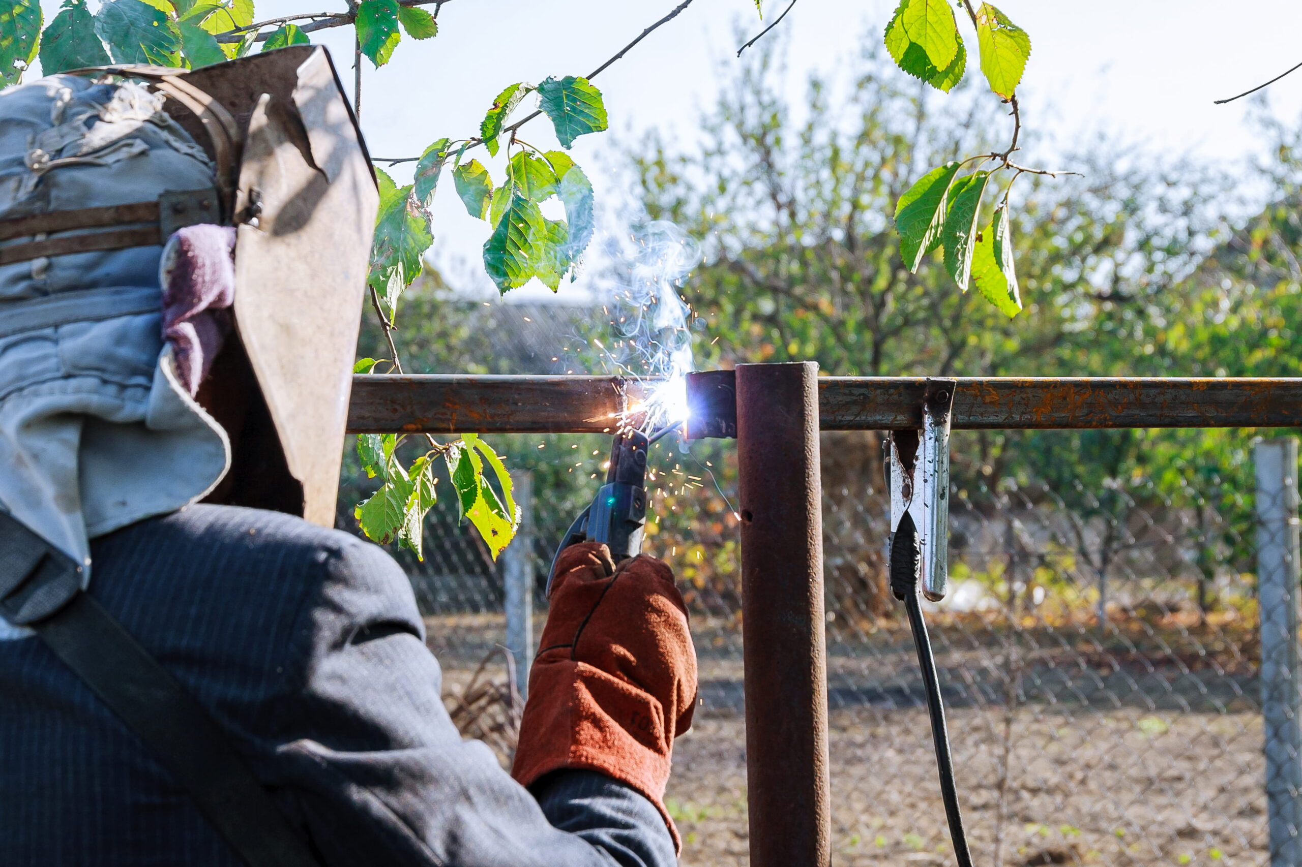 Mobile welder performing on-site welding repair on a metal fence outdoors